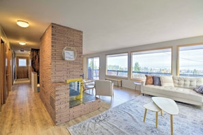 Een moderne woonkamer met een haard van baksteen, een bank, een salontafel en grote ramen met uitzicht op het buiten.