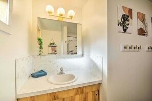 Un bagno con lavabo in marmo bianco, uno specchio con tre luci e opere d'arte appese al muro.