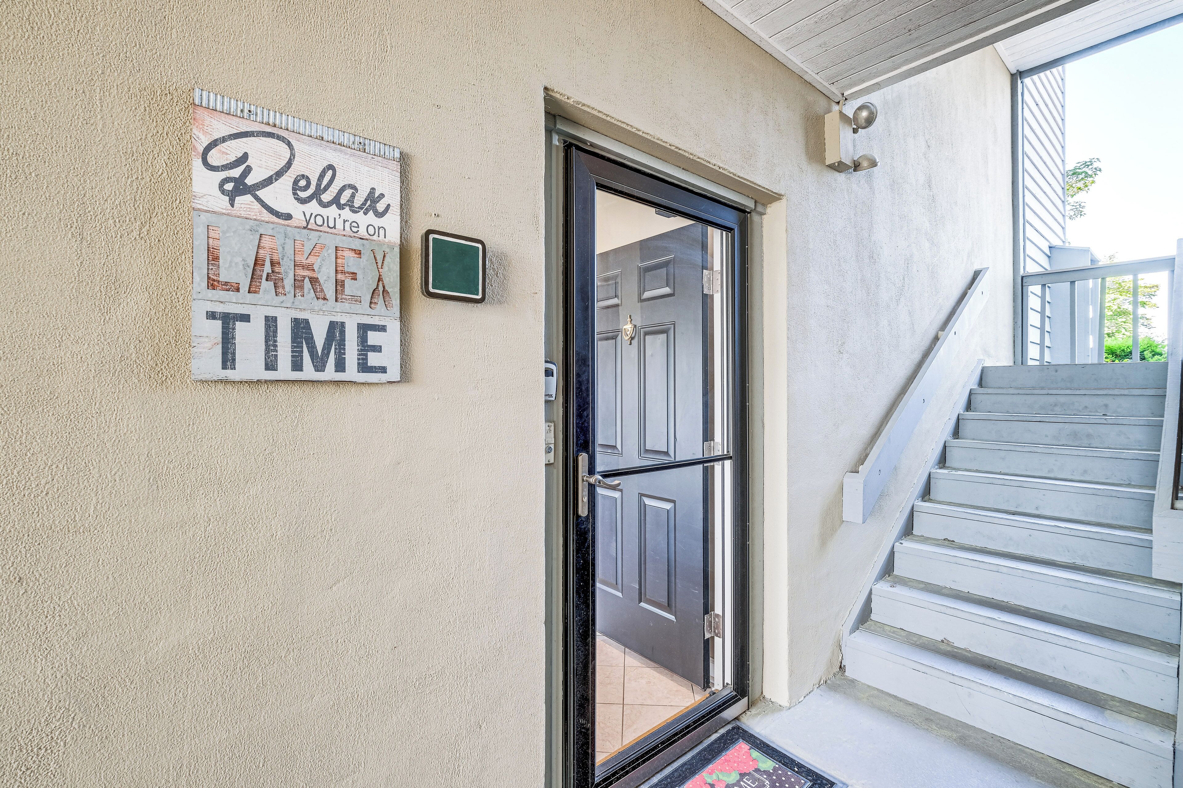 Entrada de una casa con puerta, una escalera y un letrero que dice "Relájate, estás de VACACIONES EN EL LAGO".