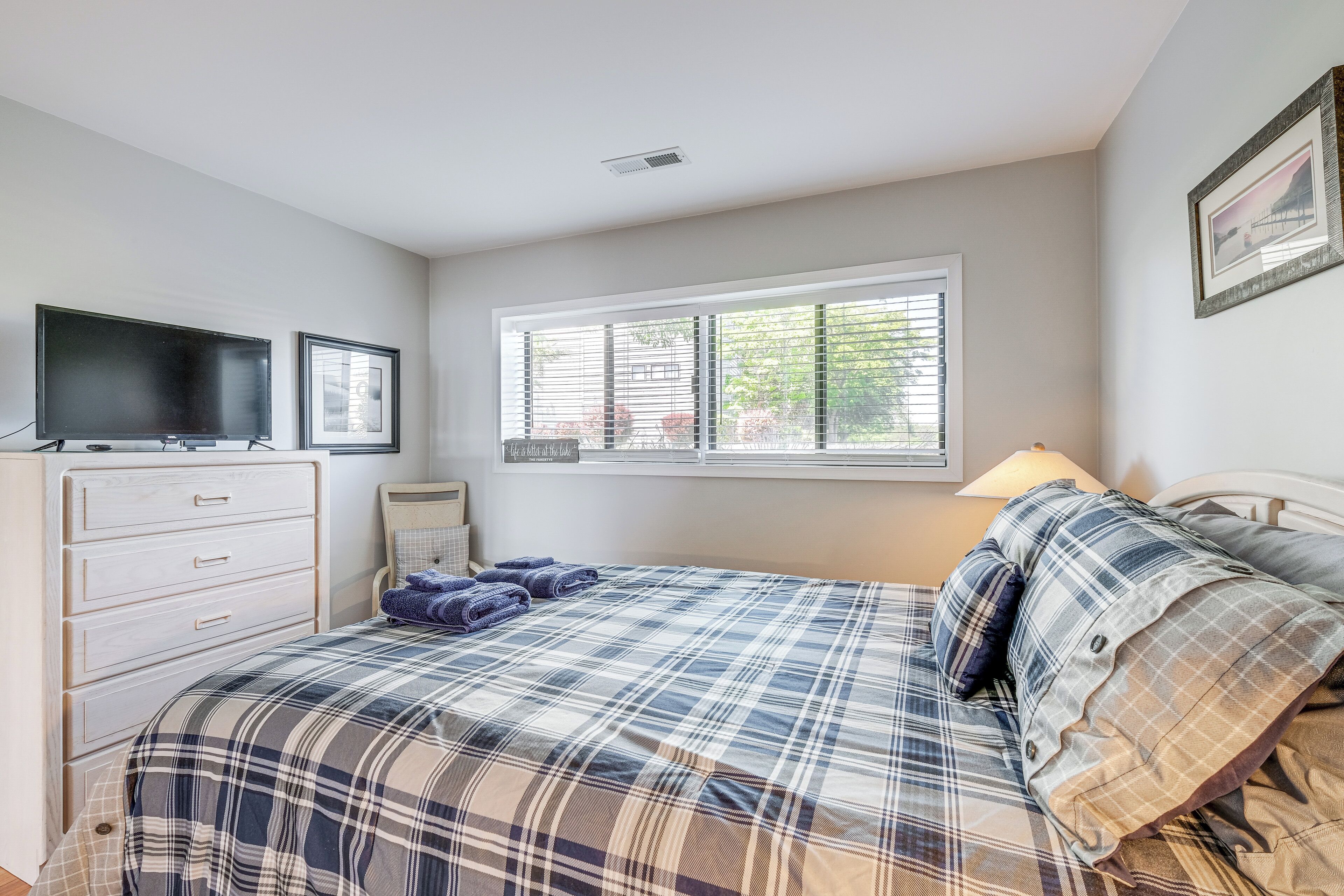 Une chambre à coucher avec un lit, une commode, un téléviseur et une fenêtre avec des stores.