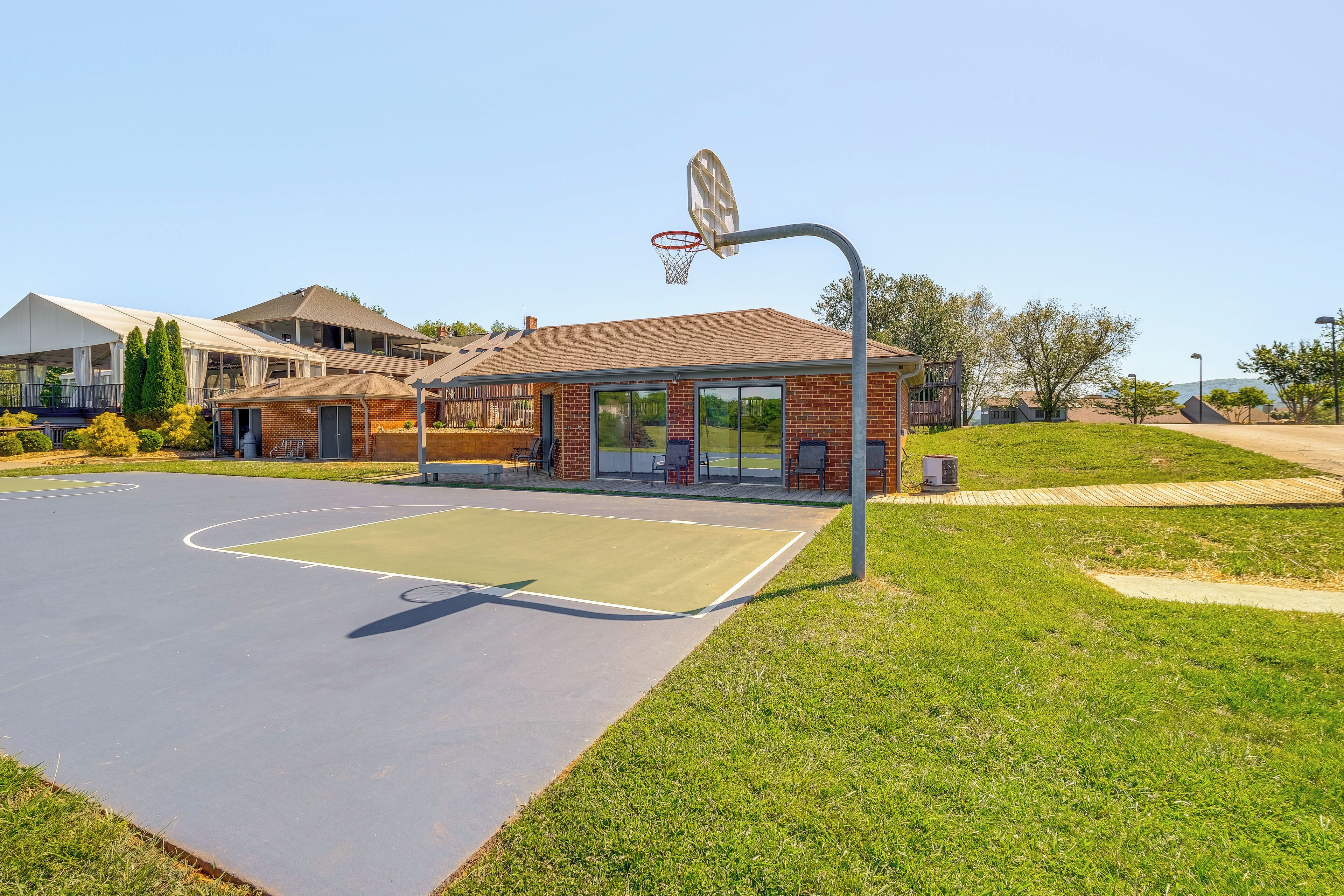 An outdoor basketball court with a hoop, surrounded by a grassy area and a building with a brick facade.