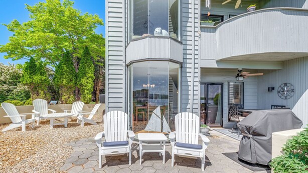 A modern two-story house with a patio area featuring white Adirondack chairs, a hexagonal stone floor, and a covered grill.