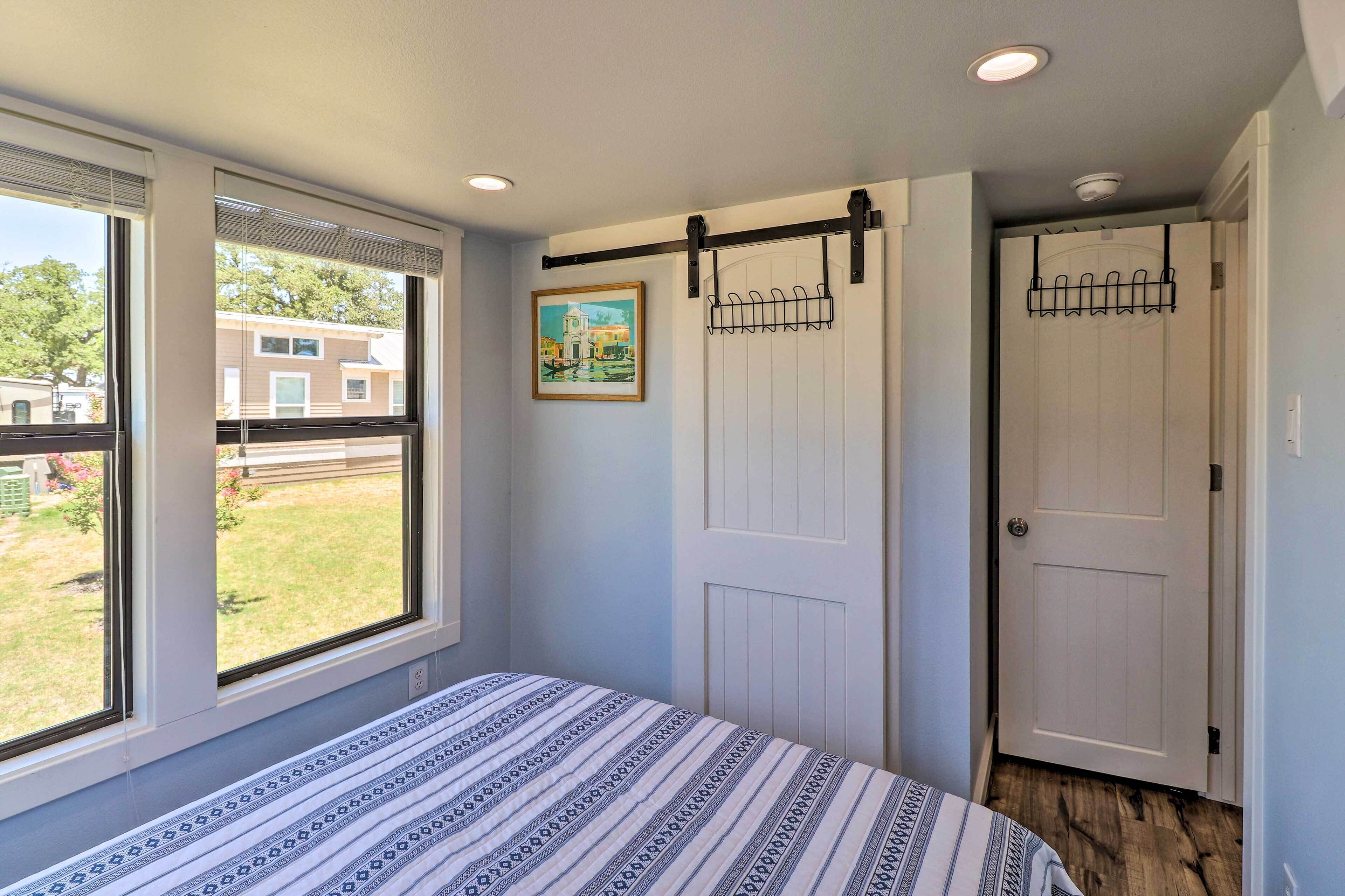 A bedroom with a bed, a window, a door, and a wall-mounted rack.