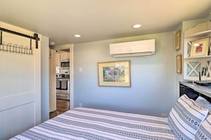 A bedroom with a bed, a wall-mounted air conditioner, a framed picture, and a kitchen in the background. - Upscale Tiny Home - Boho-chic Austin Getaway! (Austin)