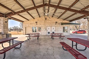 A covered picnic area with stone walls, metal benches, and a ceiling fan. - Upscale Tiny Home - Boho-chic Austin Getaway! (Austin)
