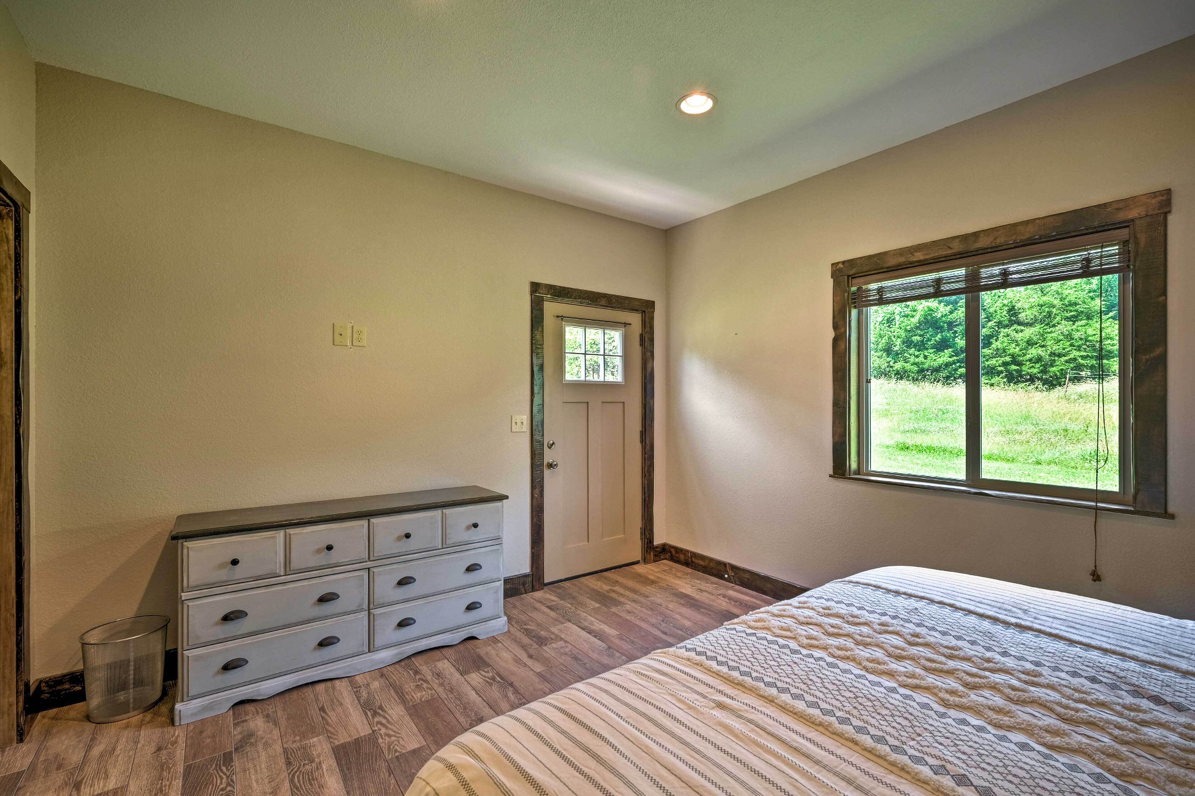 A bedroom with a bed, dresser, and a window with a view of greenery.