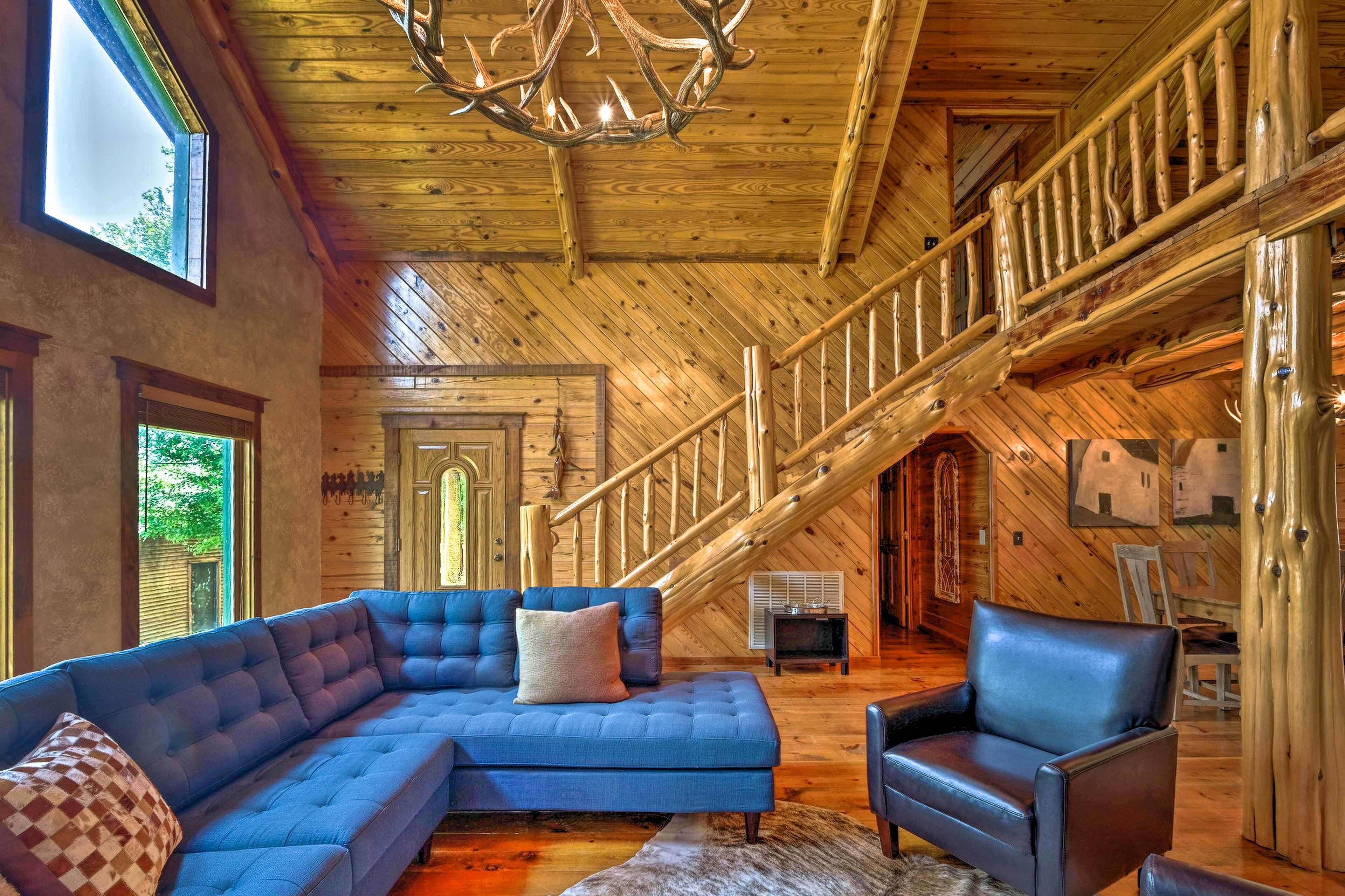 A spacious living room with a large sectional sofa, a leather armchair, and a wooden staircase.