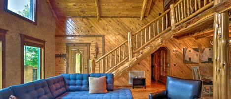 A spacious living room with a large sectional sofa, a leather armchair, and a wooden staircase.
