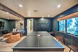 Una mesa de ping pong en una habitación con pared de piedra, un letrero de neón y vistas a árboles a través de una ventana.