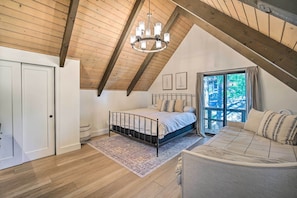 Un dormitorio con techo inclinado, una cama con cabecera, una ventana con cortinas y vistas a árboles.