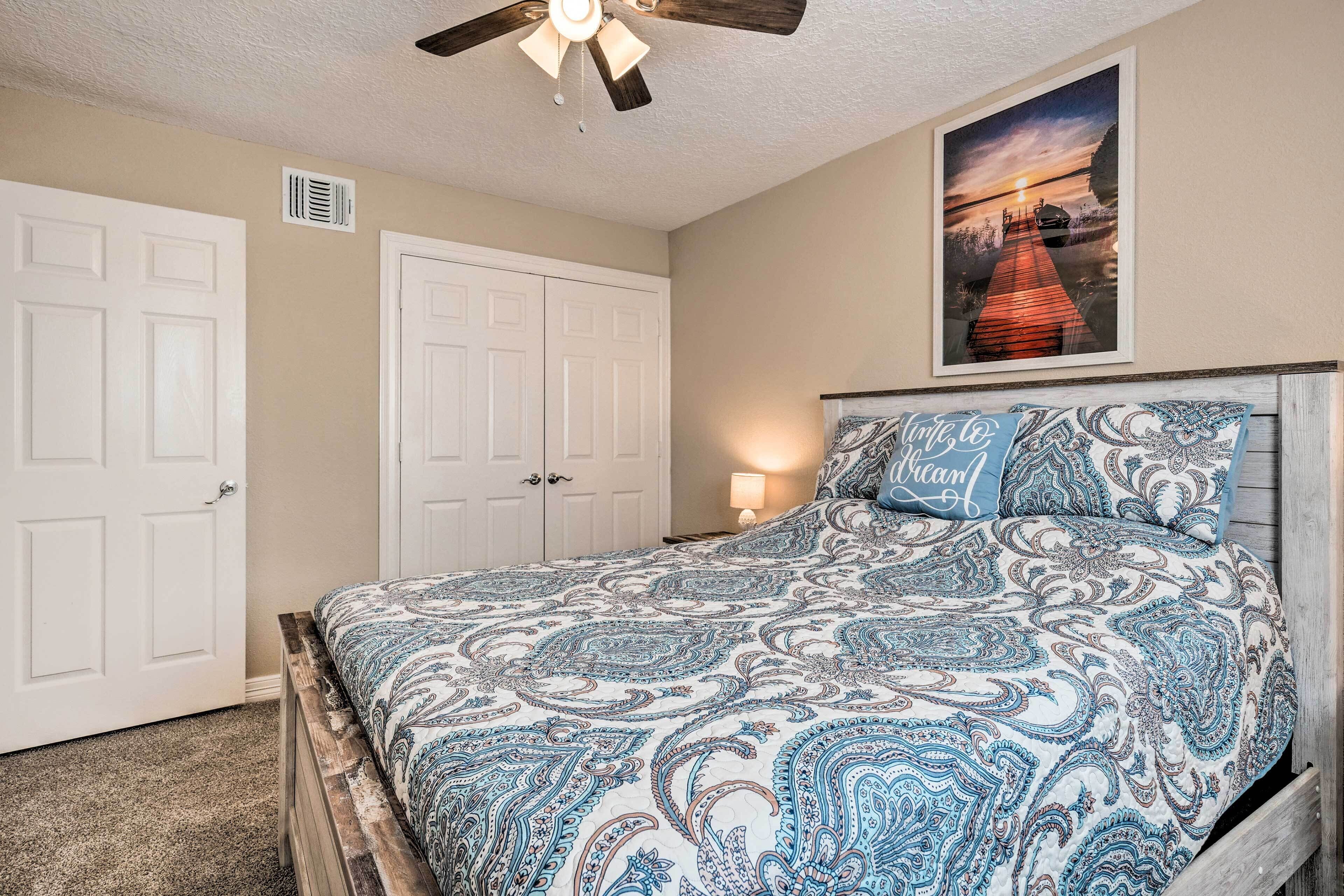 A bedroom with a bed, a ceiling fan, a nightstand with a lamp, and a door.