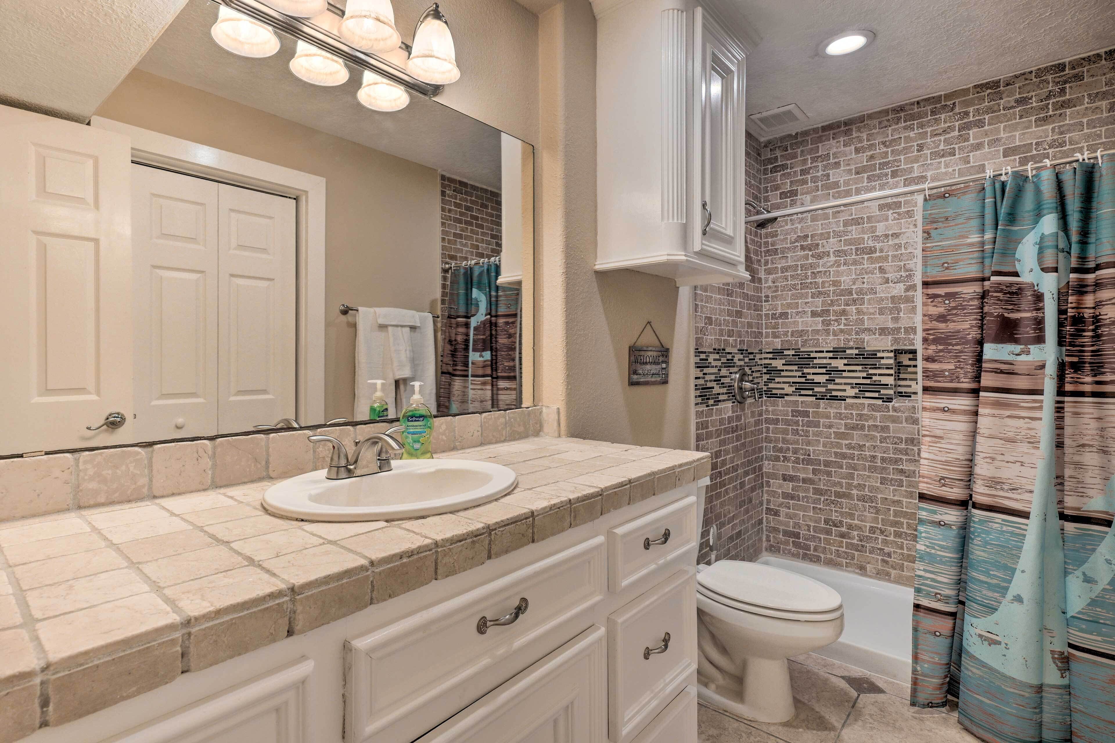A bathroom with a white vanity, a sink, a mirror, a toilet, and a shower with a brick wall and a curtain.
