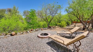 Eine Terrasse mit Feuerstelle, Liegestühlen und Kiesfläche, umgeben von Grünpflanzen.