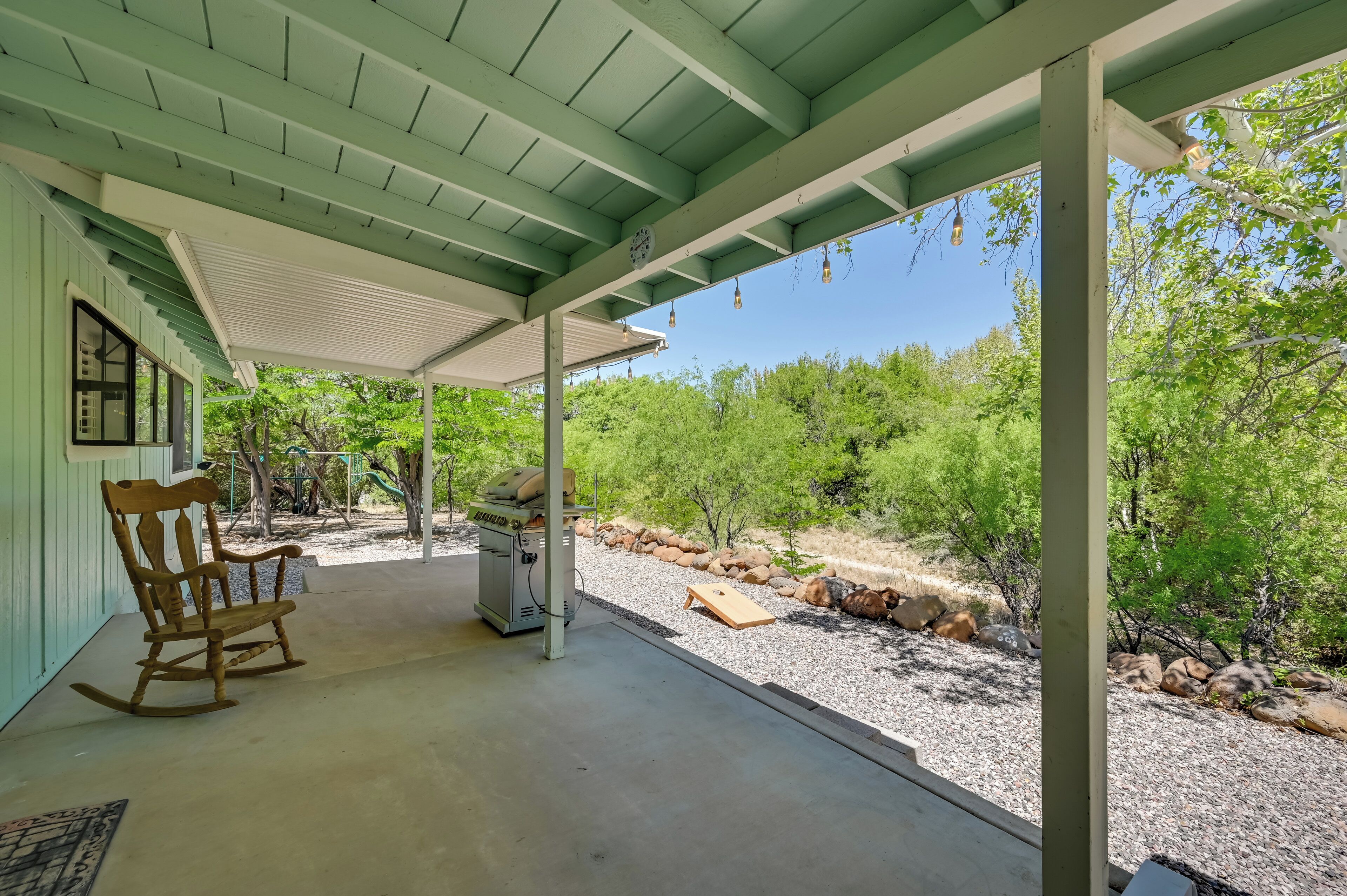 A covered porch with a rocking chair, a grill, and a view of a rocky landscape with trees.