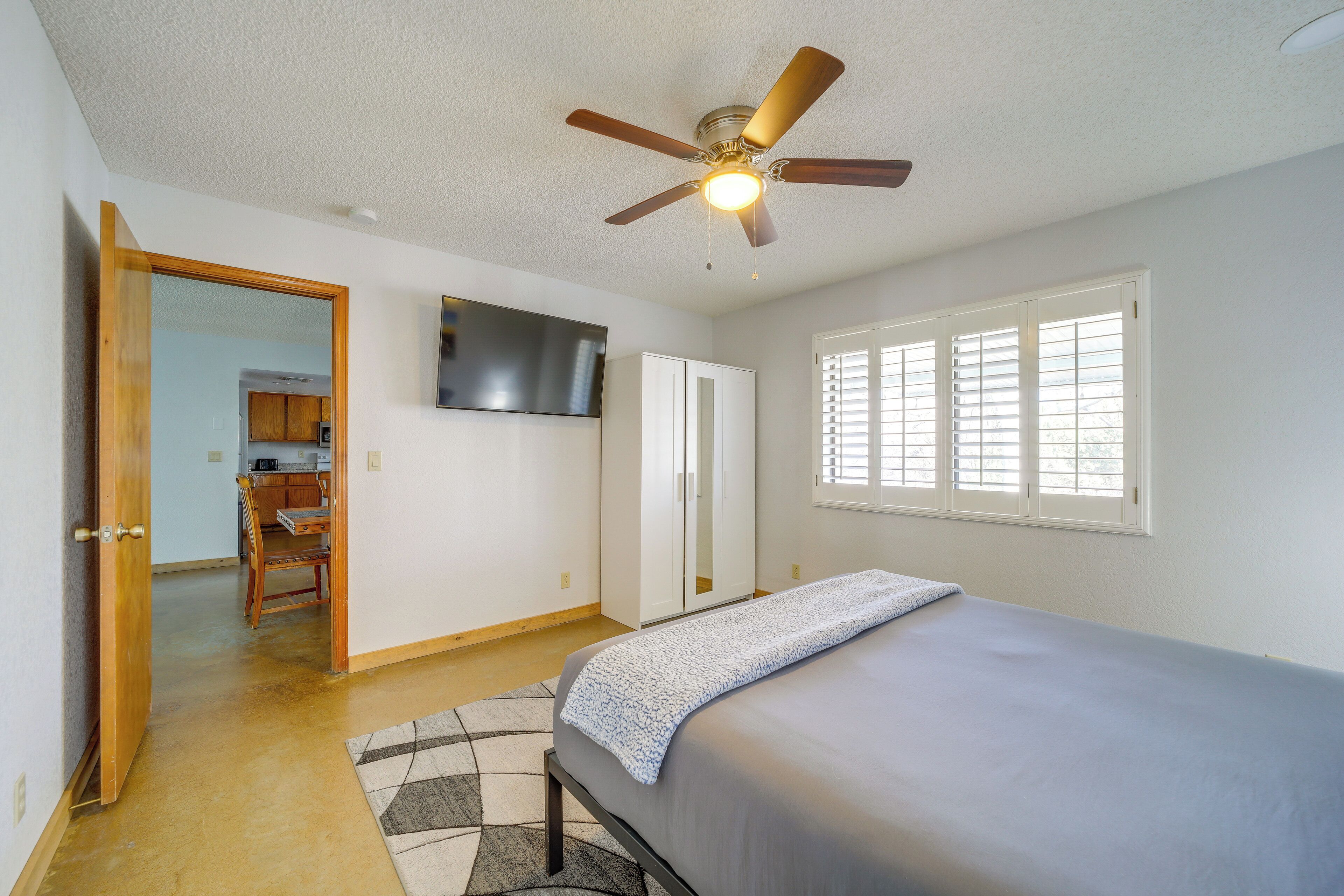 A bedroom with a bed, a ceiling fan, a TV mounted on the wall, and a window with blinds.