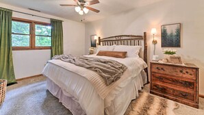 Un dormitorio con una cama, un aparador de madera, un ventilador de techo, una ventana con cortinas y una lámpara de pared.