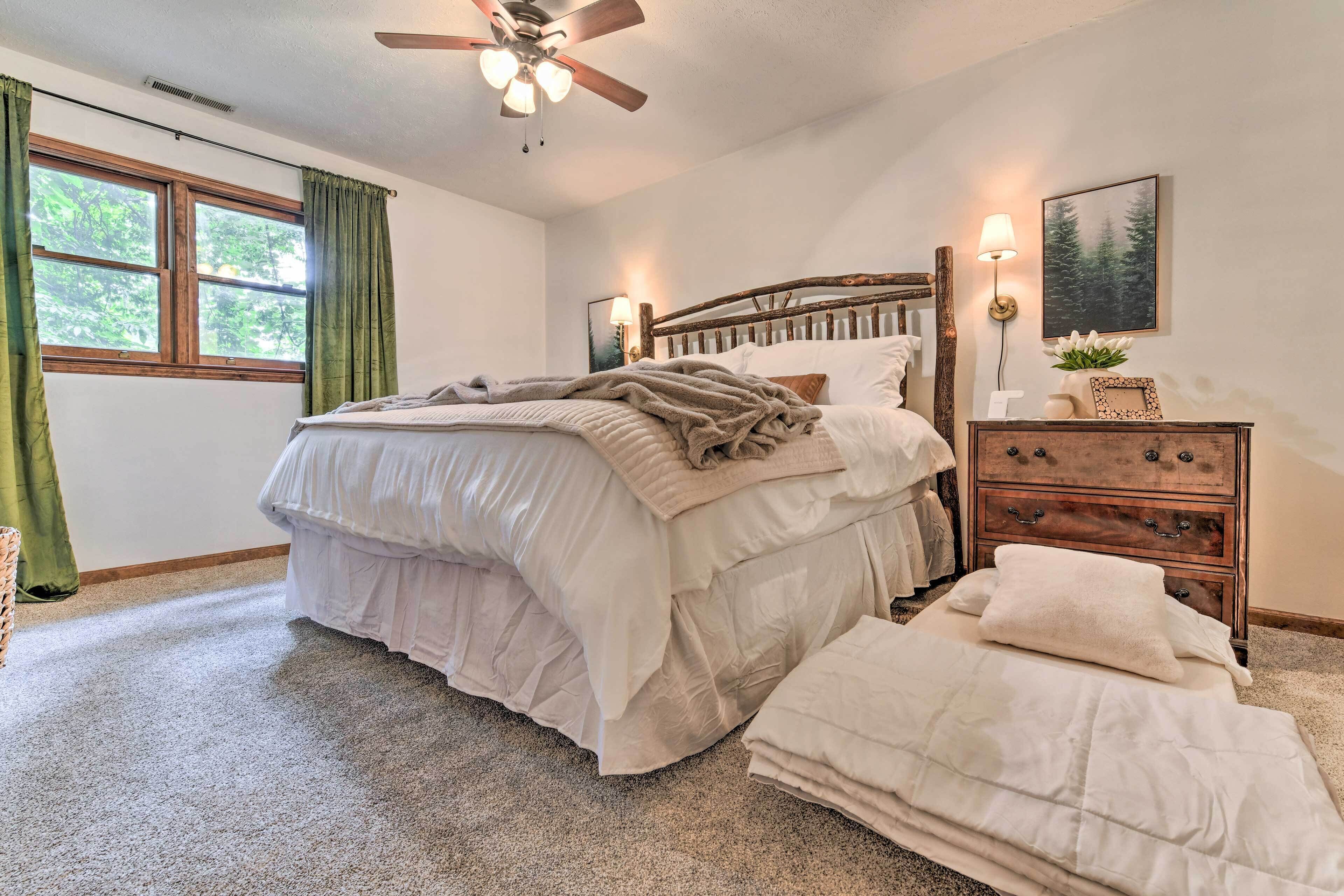 A bedroom with a bed, a dresser, a ceiling fan, a window with curtains, and a wall-mounted lamp.