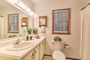 A bathroom with a sink, mirror, toilet, and two windows with blinds. - Maggie Valley Townhome In Smoky Mountain Foothills (Waynesville)