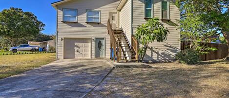 A two-story house with a front garage, a wooden staircase, and a small front yard with a tree.