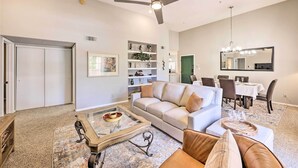 A living room with a white sofa, a coffee table, and a chandelier. There is a dining area with a table and chairs. - Modern Scottsdale Condo ~ 10 Mi to Old Town! (Scottsdale)