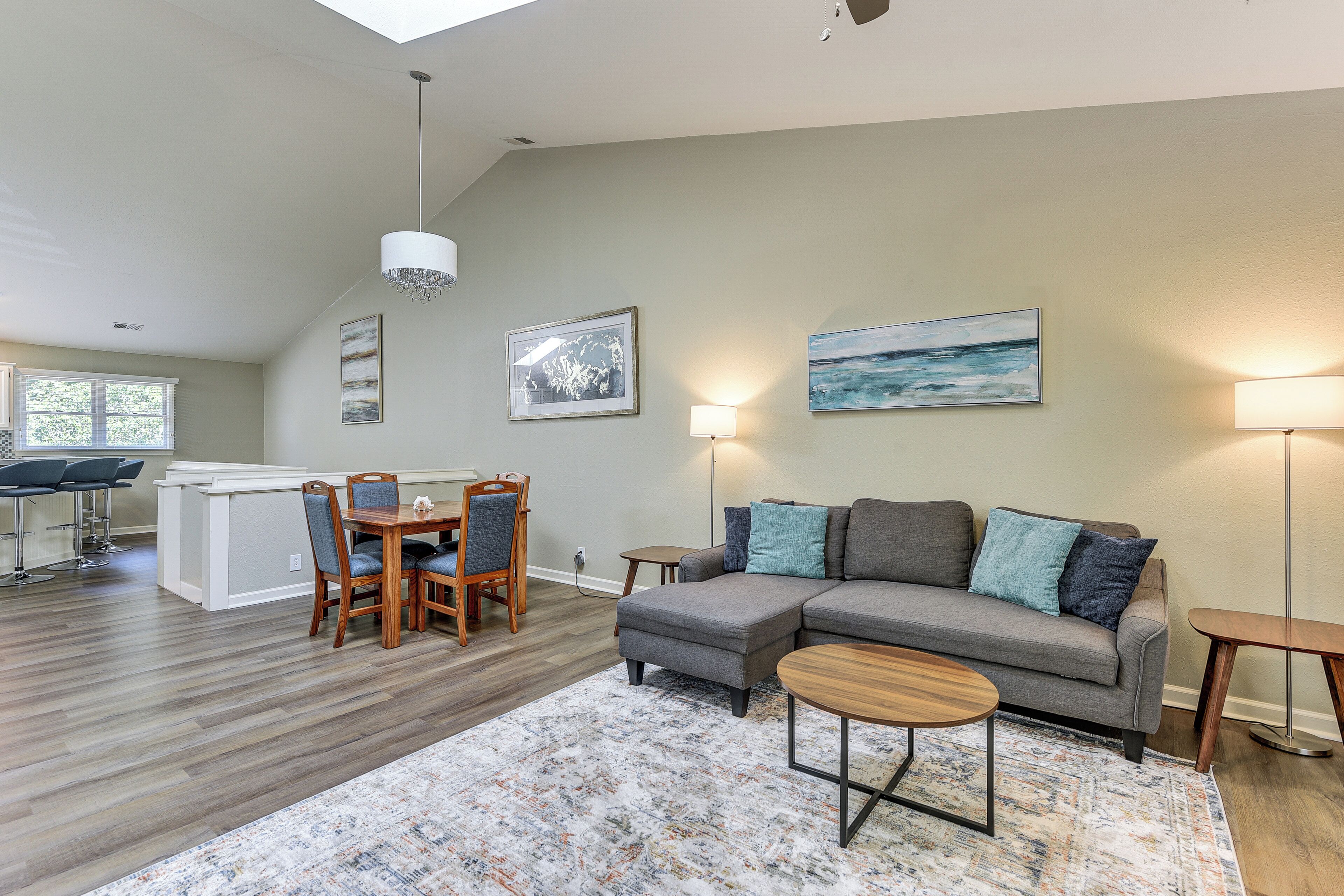 A modern living room with a sectional sofa, a dining area with a wooden table and chairs, and a kitchen in the background.