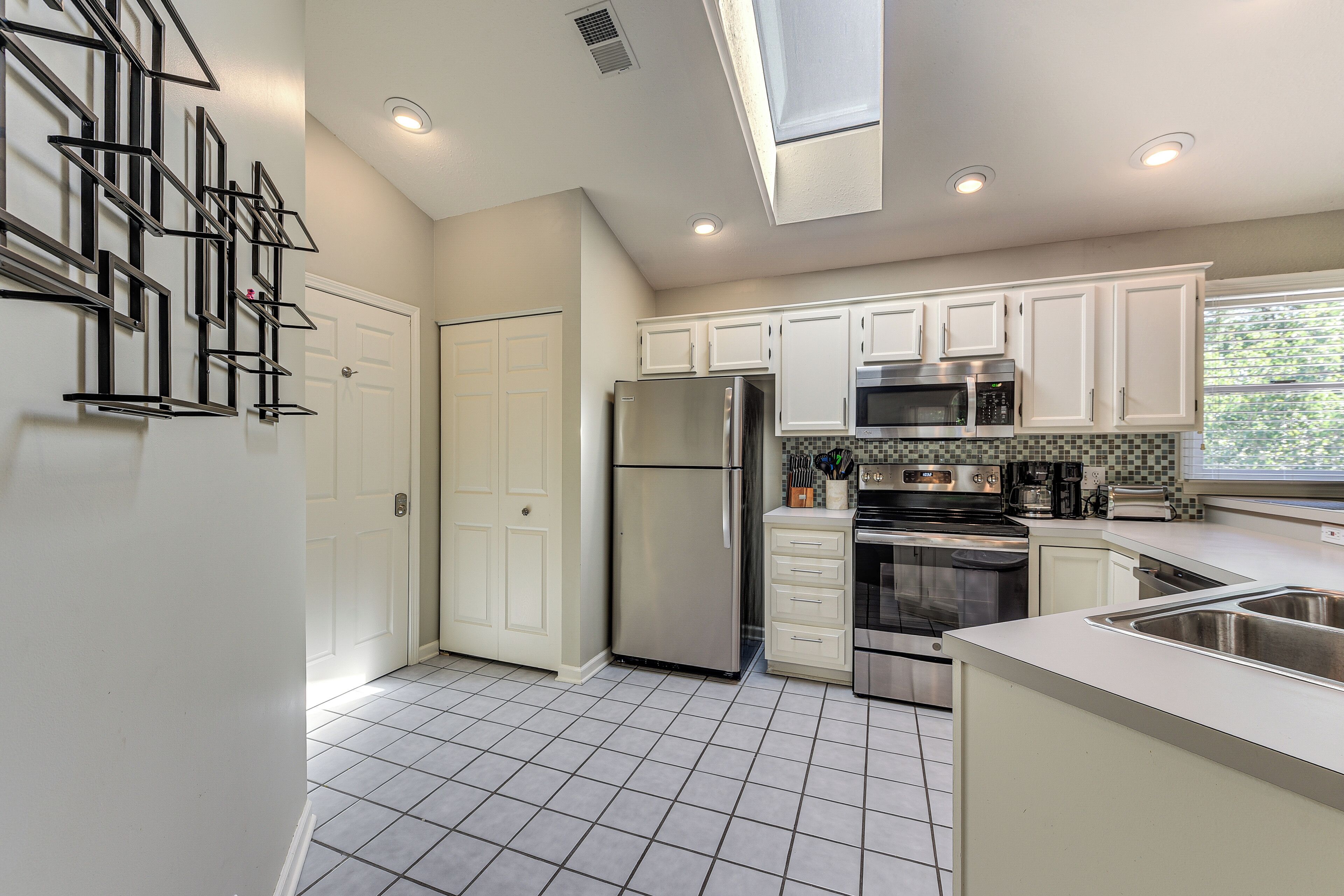 A modern kitchen with white cabinets, stainless steel appliances, and a tiled floor.