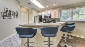 A modern kitchen with a central island, bar stools, and a skylight. - Resort Condo ~ 2 Mi to Sunset Beach Seashore! (Sunset Beach)