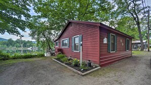 A small, red wooden cabin with a dirt ground, surrounded by trees and a body of water in the background. - Riverfront Escape w/ Dock: 19 Mi to Saratoga! (Lake Luzerne)
