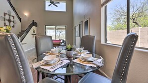 A dining area with a glass table set for four, surrounded by leather chairs, a ceiling fan, and a view of the outdoors through a large window.