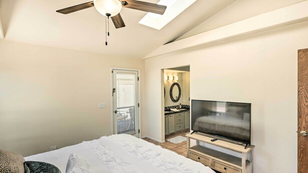 Ein Schlafzimmer mit einem Bett, einem Fernseher auf einem Schrank, einem Deckenventilator und einem durch eine offene Tür einsehbaren Badezimmer.