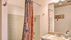 Un baño con bañera, cortina de ducha, lavamanos con espejo y un armario azul.