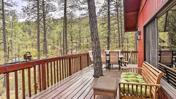 Una terraza de madera con un banco y una mesa, rodeada de árboles.