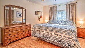 Un dormitorio con cómoda de madera, cama con ropa de cama estampada, ventilador de techo y ventana con cortinas.