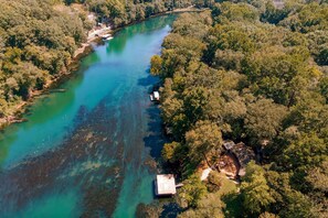 An aerial view of a river with clear water, surrounded by dense forest. There are small buildings along the riverbank. - Riverfront Retreat w/ Fire Pit: Fish & Hike! (Heber Springs)