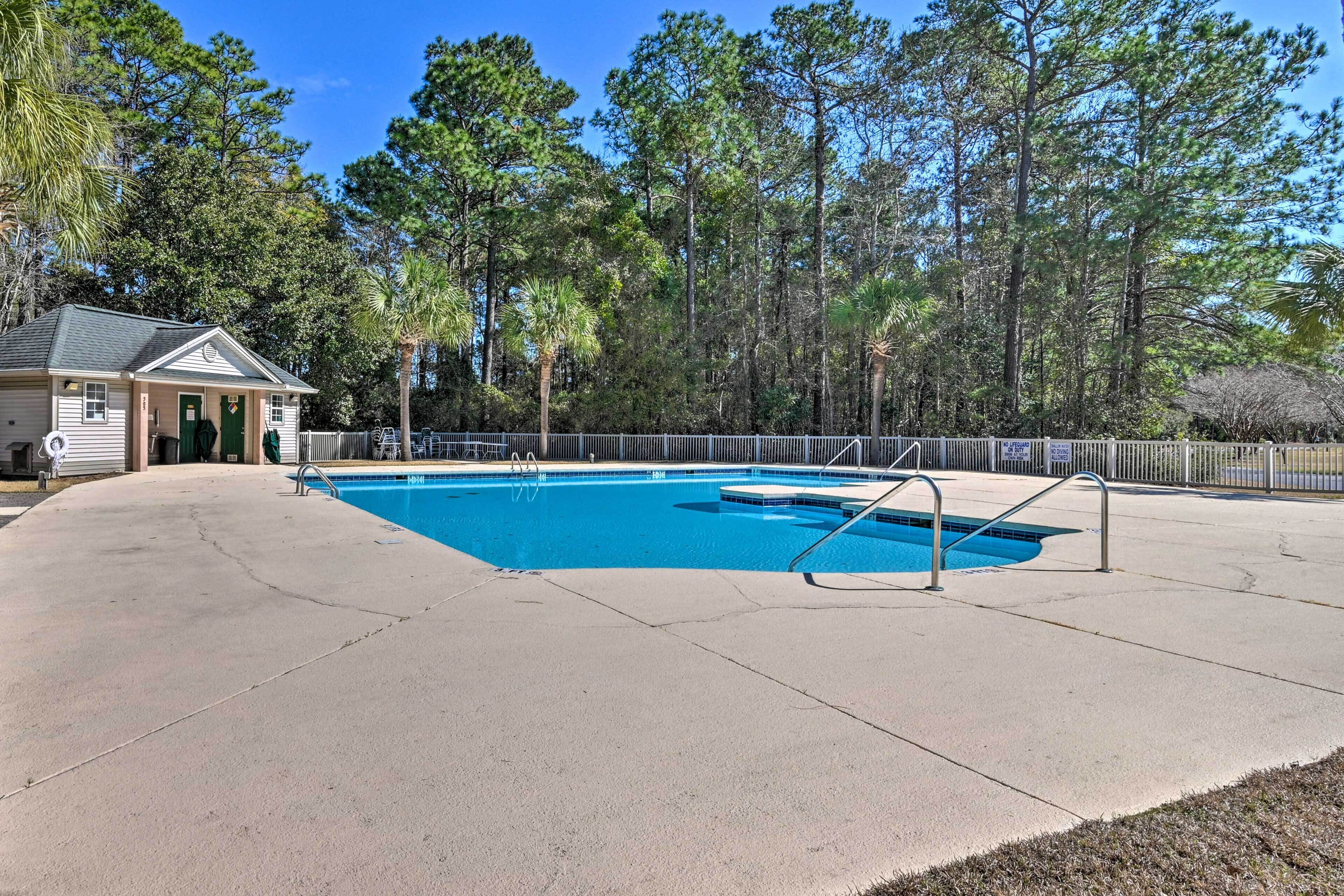 A swimming pool with a concrete deck, surrounded by a fence and trees.