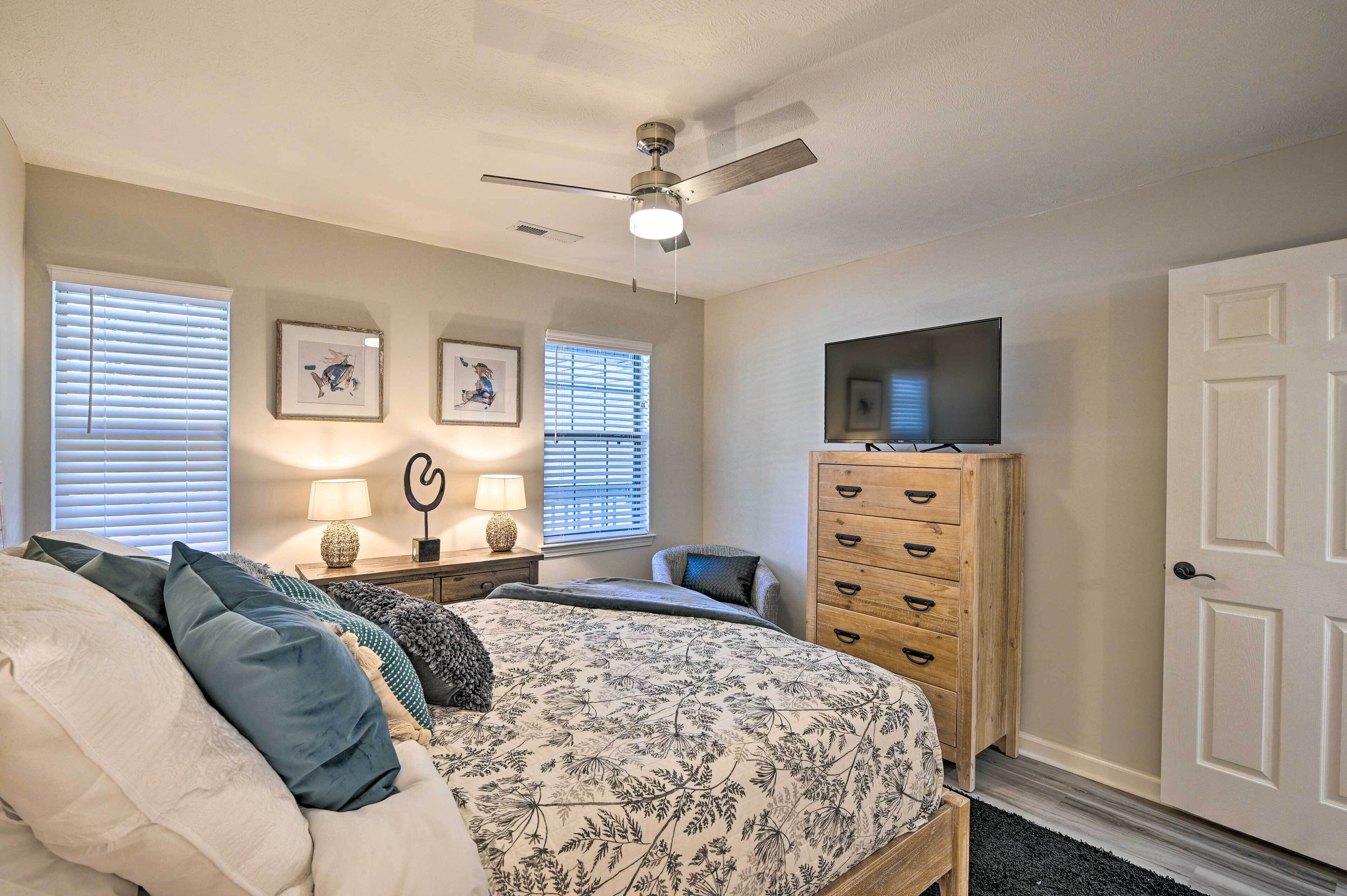 A bedroom with a bed, dresser, ceiling fan, and artwork on the walls.