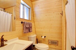 Baño de cabaña de madera con lavamanos, inodoro y ventana.