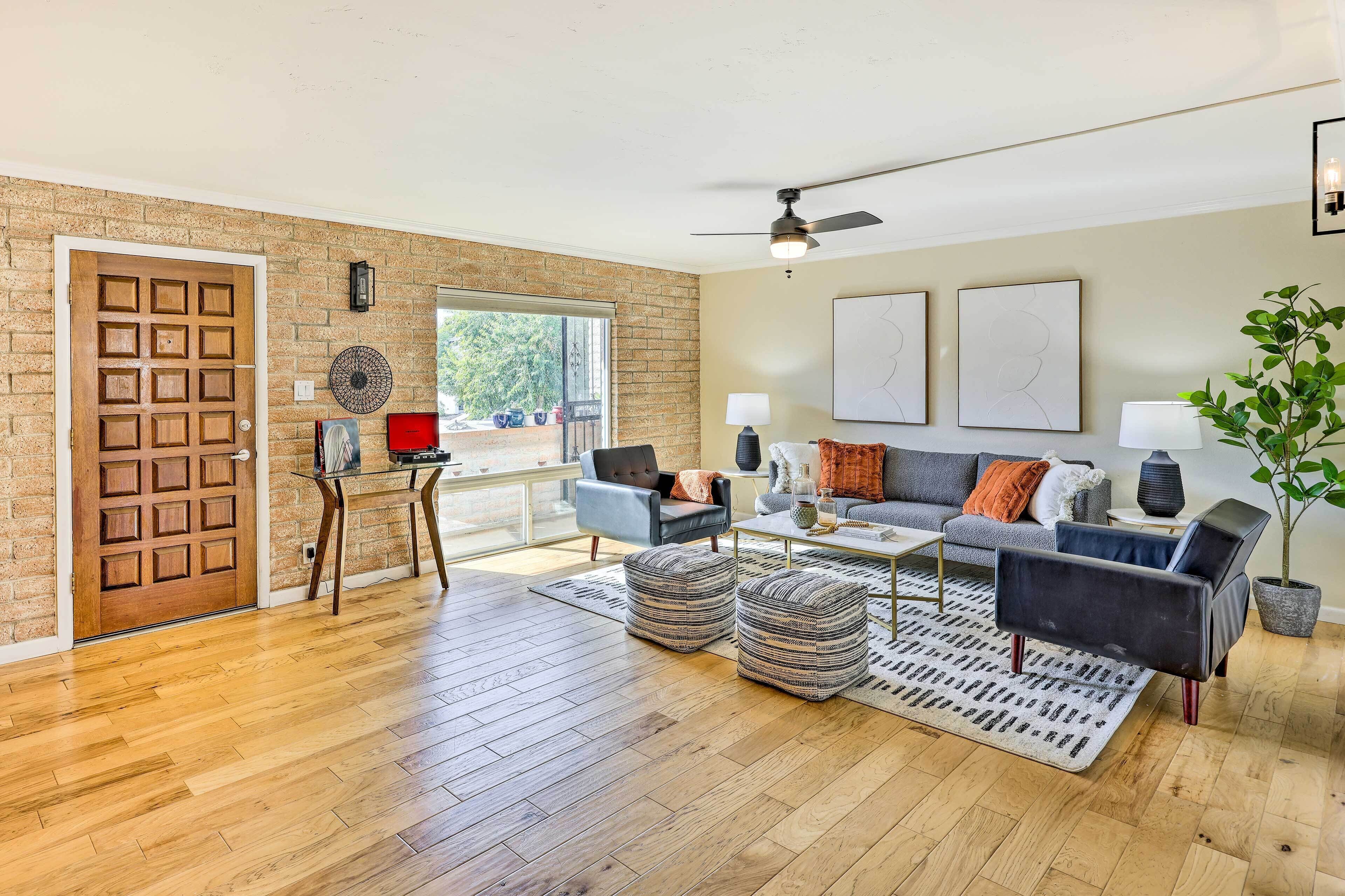 Un salon spacieux doté d’un plancher en bois, d’un mur en briques, d’un ventilateur de plafond et d’une grande fenêtre.