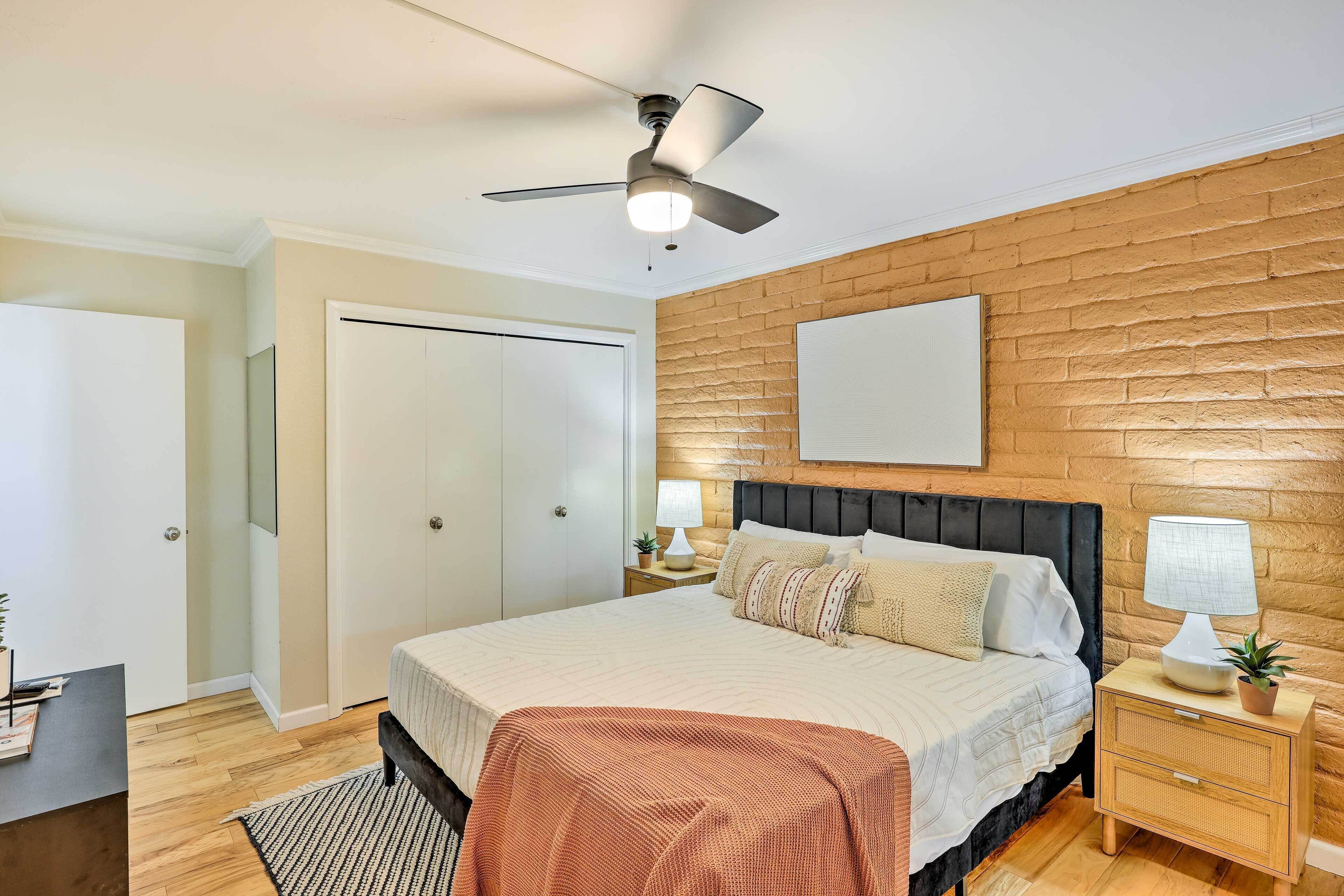 Un dormitorio con cama, mesitas de noche, ventilador de techo, una pared de acento de madera y una puerta.
