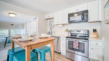 Una cocina con armarios blancos, un horno de acero inoxidable, un microondas y una mesa de madera con taburetes azules.