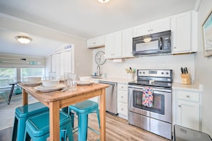 A kitchen with white cabinets, a stainless steel oven, a microwave, and a wooden table with blue stools.