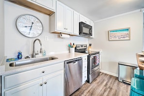 A kitchen with white cabinets, stainless steel appliances, a clock, and a framed picture on the wall.