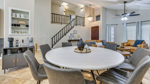Een ruime woonkamer met een ronde eettafel, grijs gestoffeerde stoelen, een trap en een koffiehoek.