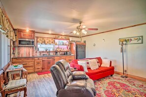 A cozy living room with a red sofa, a leather chair, and a dining table with a bowl of fruit.