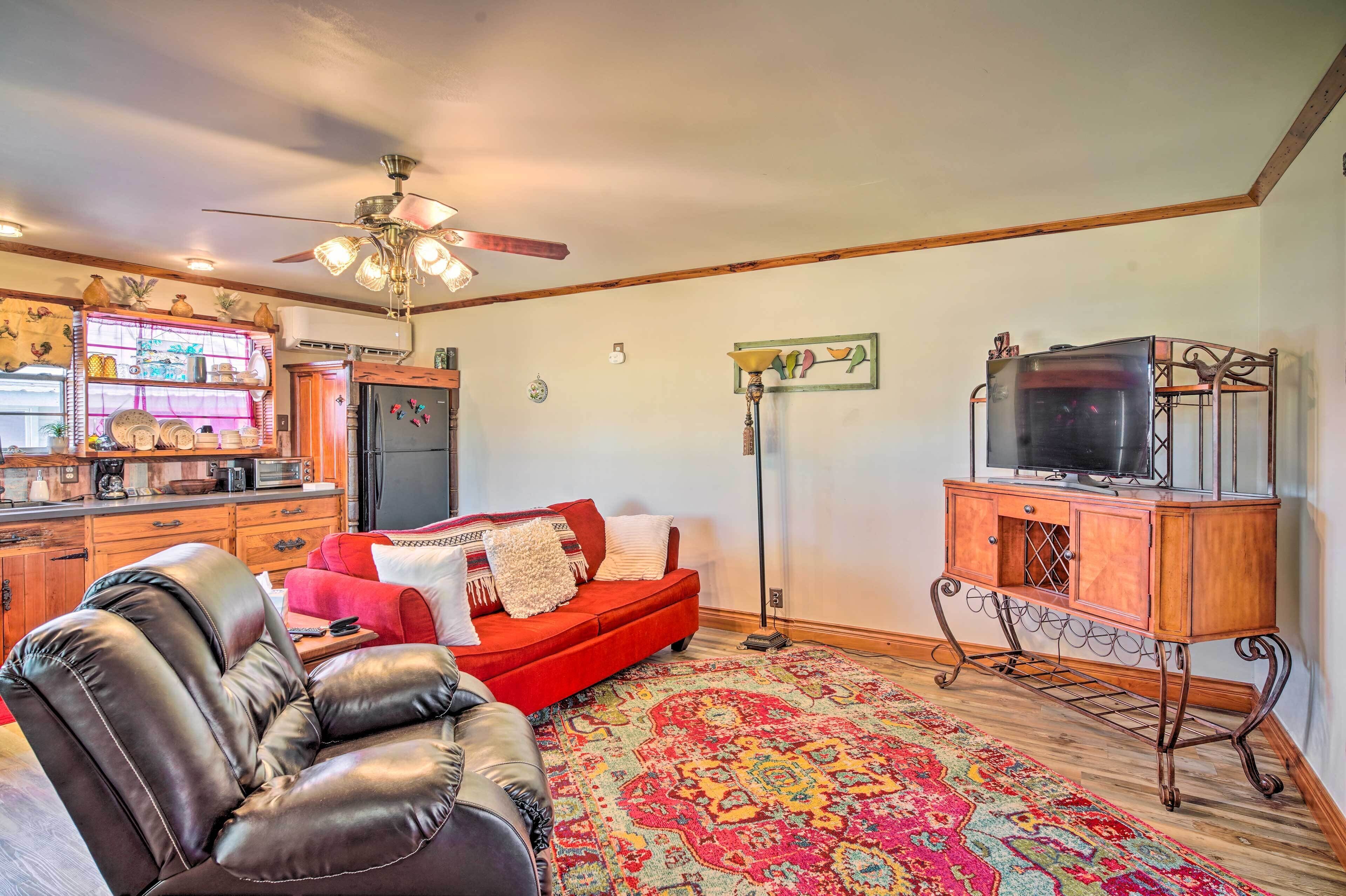 A living room with a red sofa, a leather chair, a television on a wooden stand, and a colorful rug.