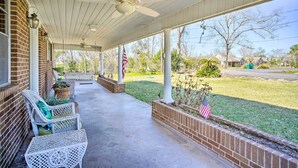 A covered porch with a ceiling fan, white wicker furniture, and an American flag. - Cozy Lake Charles Studio w/ Golf Course Views (Lake Charles)