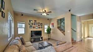 A spacious living room with a large TV, comfortable seating, a ceiling fan, and a staircase leading to another level. - 2-story Surprise Getaway w/ Patio + Fire Pit! (Surprise)