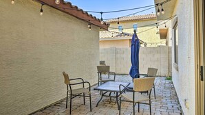 A patio with a table and chairs, string lights, and a blue umbrella. - 2-story Surprise Getaway w/ Patio + Fire Pit! (Surprise)