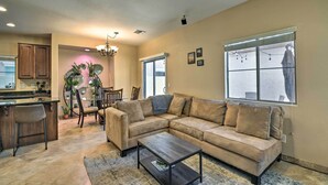 A living room with a beige sofa, a coffee table, and a dining area with chairs and a chandelier. - 2-story Surprise Getaway w/ Patio + Fire Pit! (Surprise)