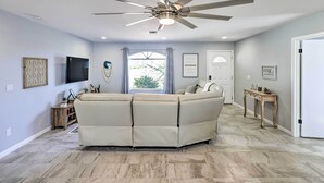 A modern living room with a sectional sofa, ceiling fan, flat-screen TV, and a view to the outdoors. - Heated Pool: Home ~ 5 Mi to Lake Havasu! (Lake Havasu City)
